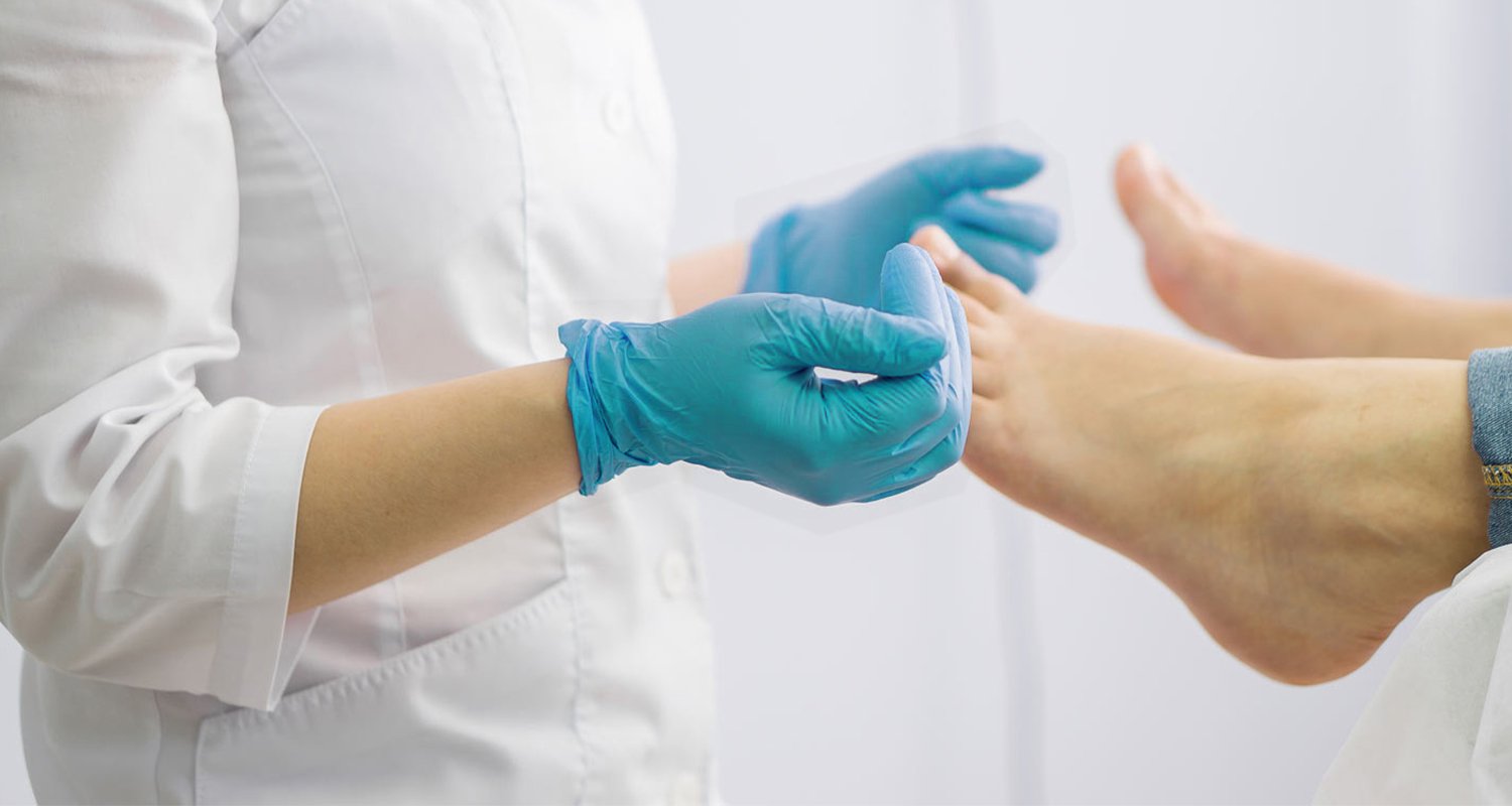 manos con guantes de podóloga sostienen a un pie desde las uñas